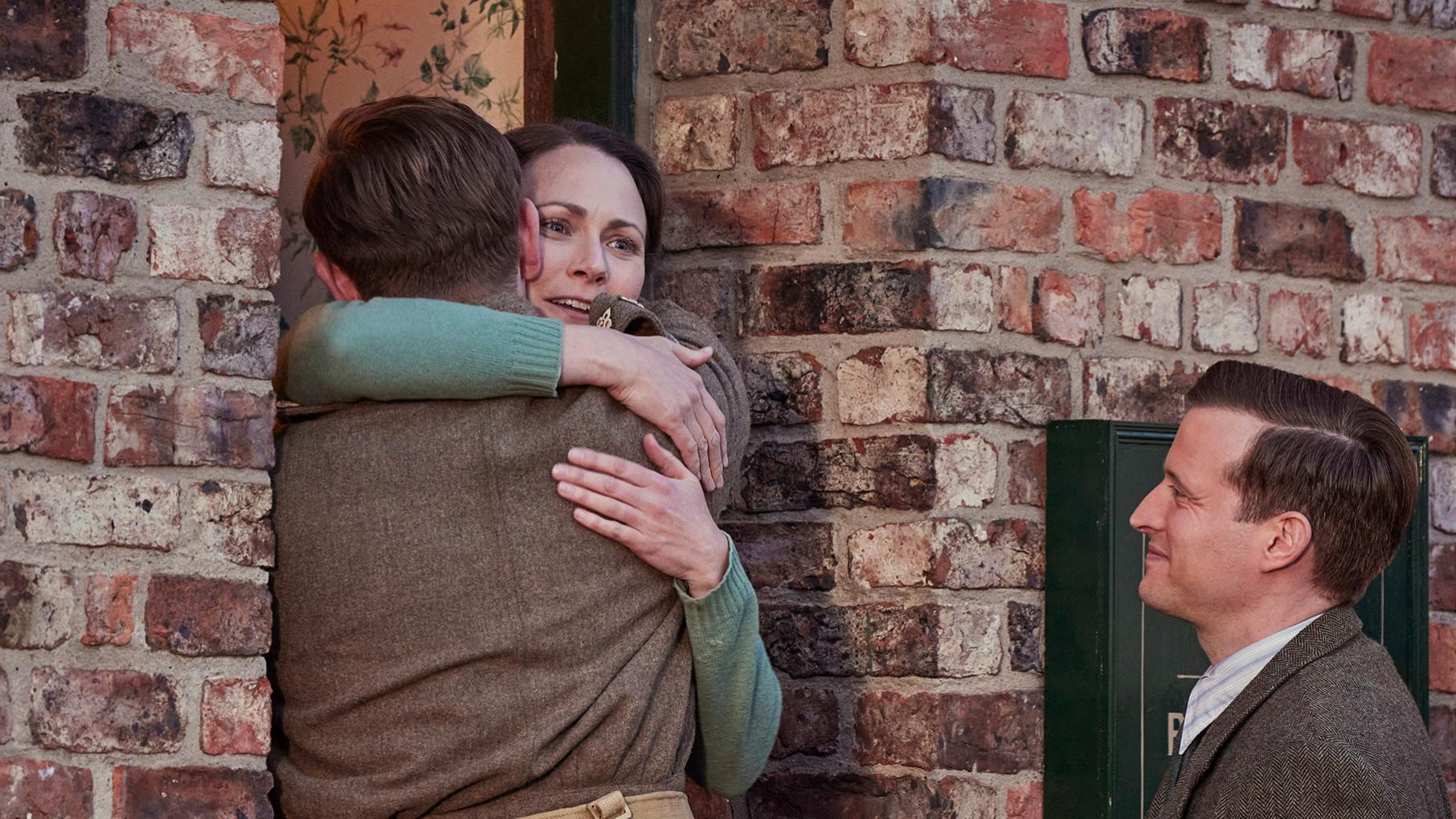 Tristan hugs Mrs. Hall in a doorway while James looks on smiling