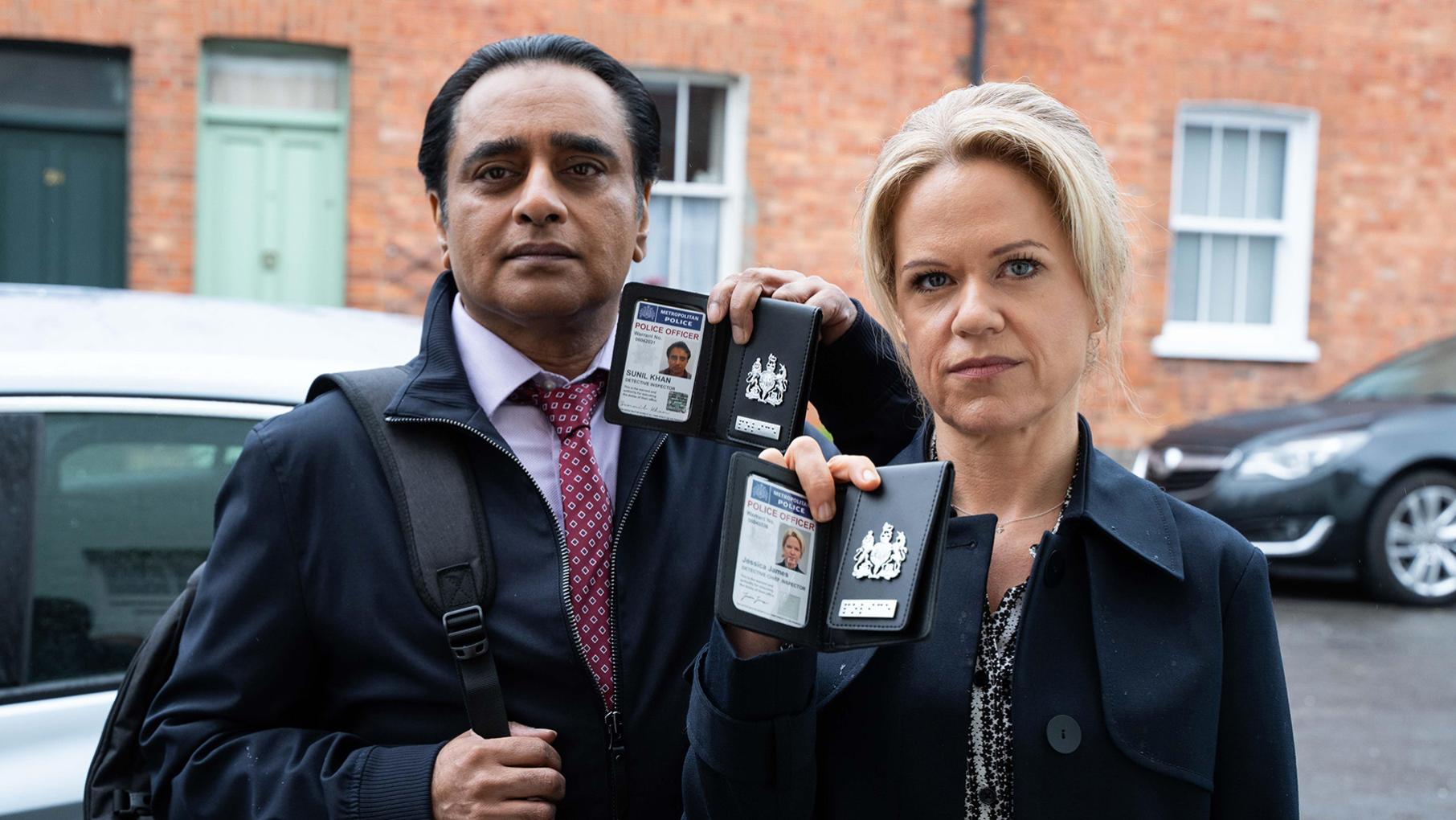 Sunny and Jess stand outside holding up police badges