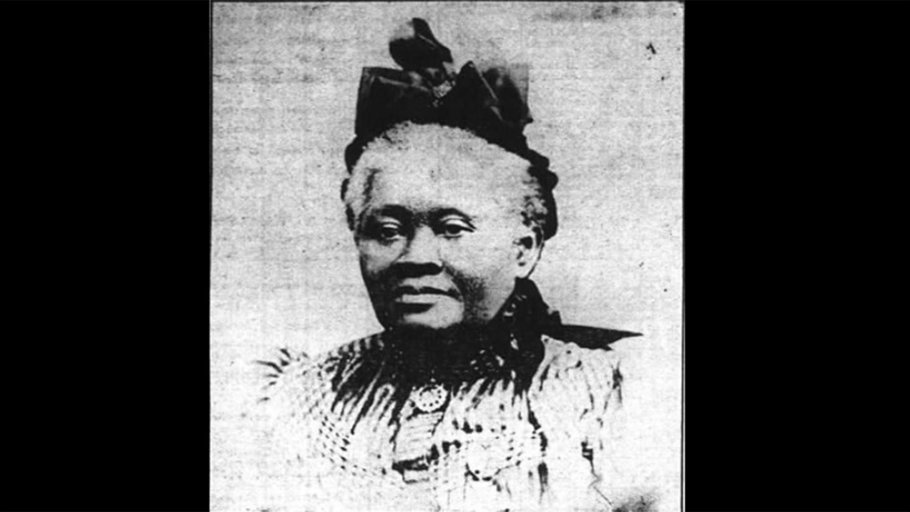 A black and white newspaper image of a Black woman in a gown with a hat