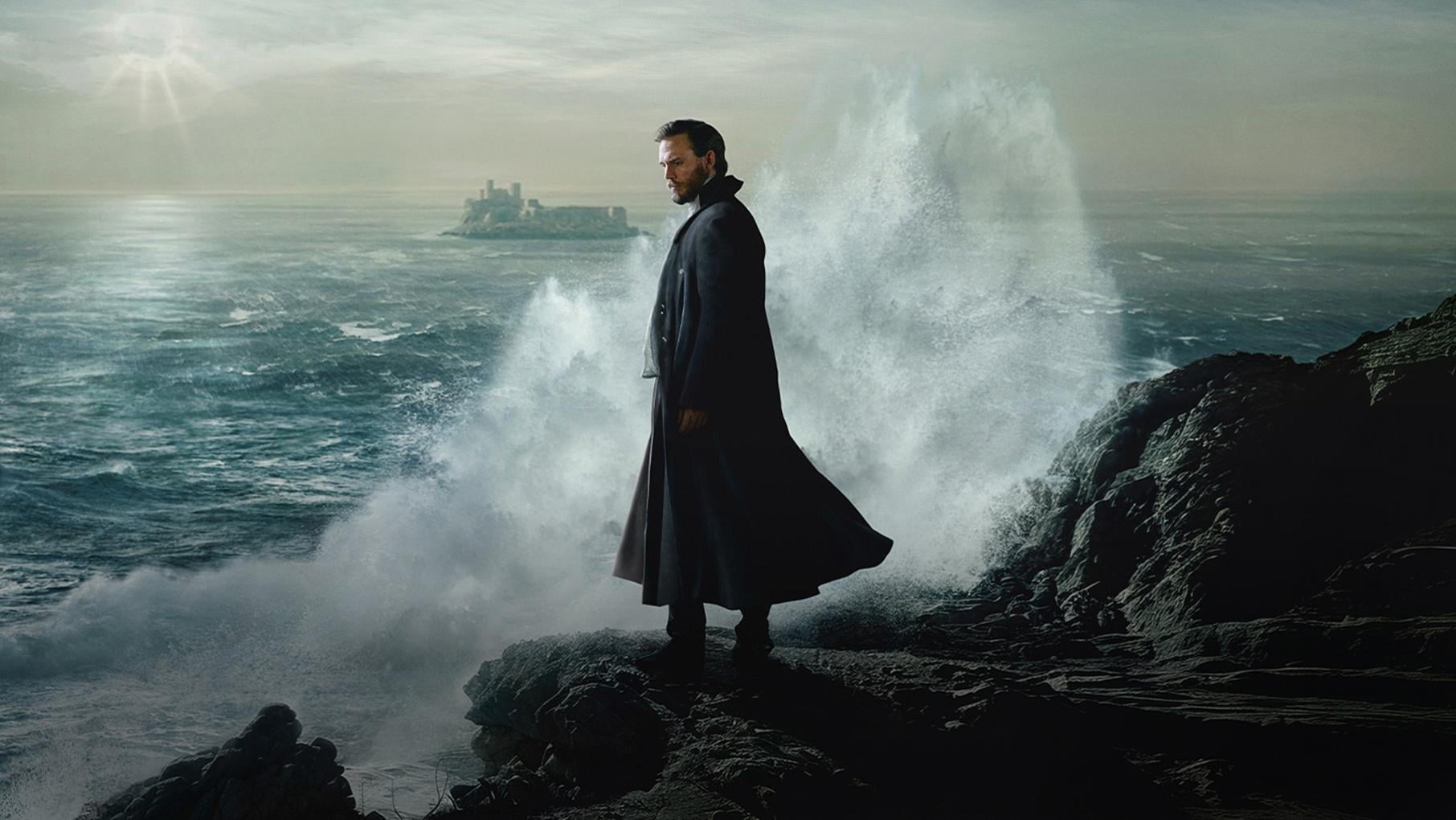 A man stands on a cliff in front of a dramatic wave breaking on the rocks