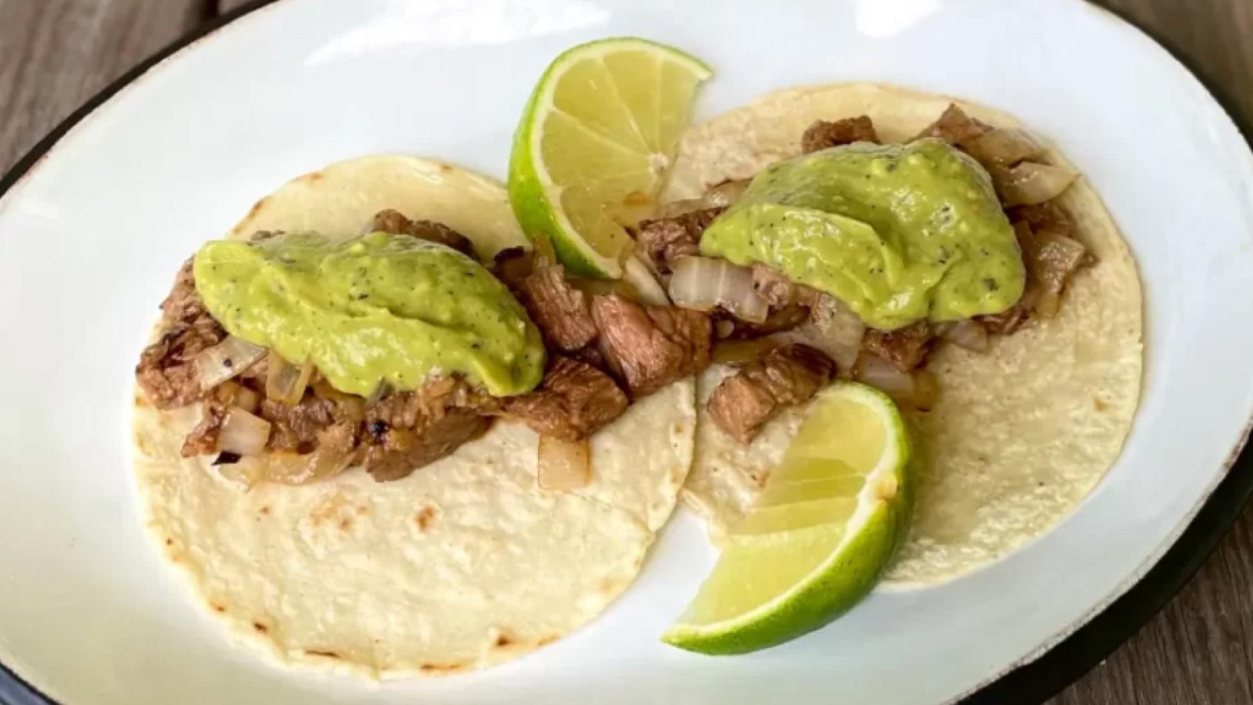 Two tacos with steak, a green sauce, and lime wedges on a plate