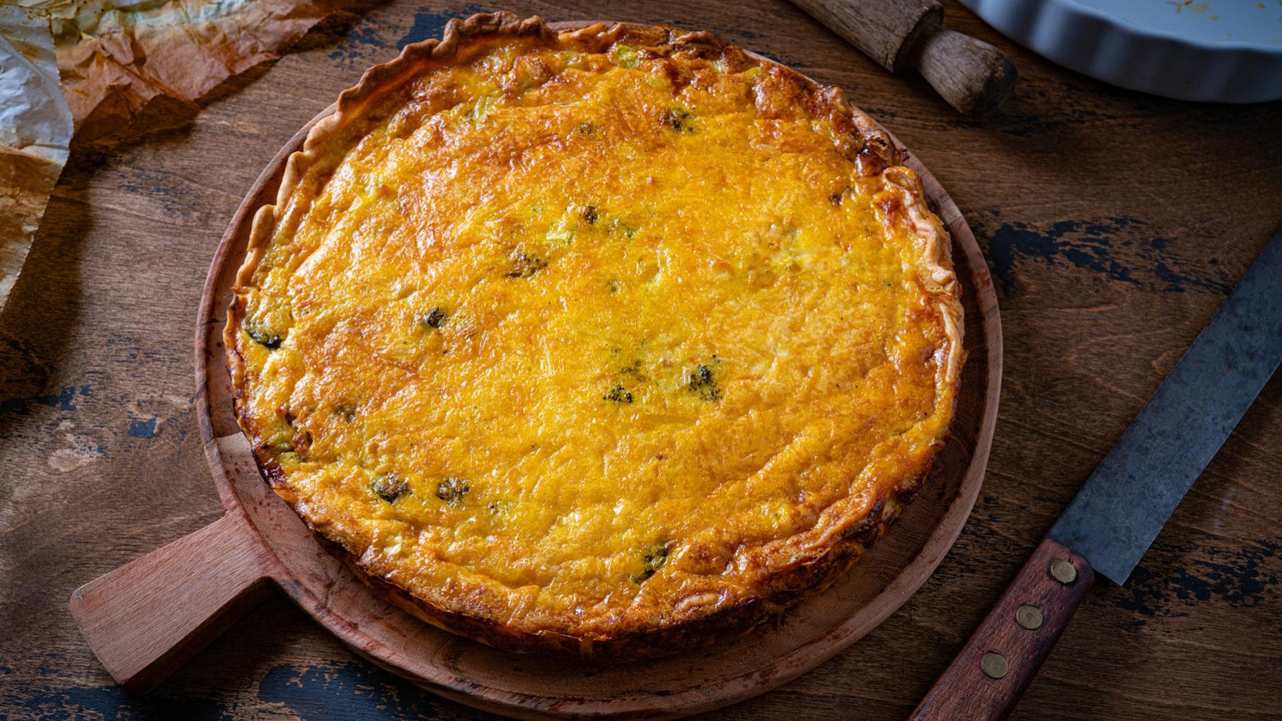 A broccoli cheddar quiche in a pan on a wooden table