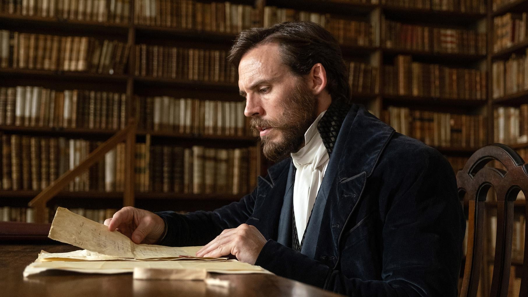 Edmond sits in a nice jacket in a library reading an old letter