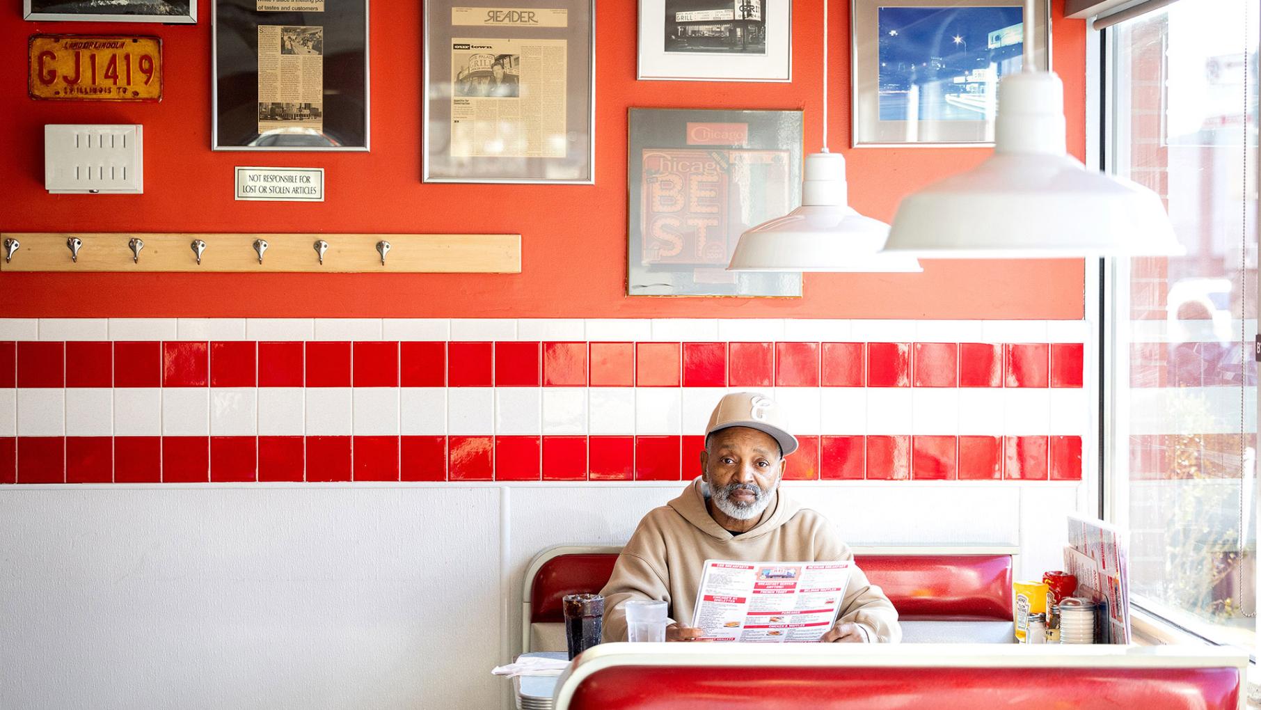 A man in a baseball cap sits against the wall in a diner booth