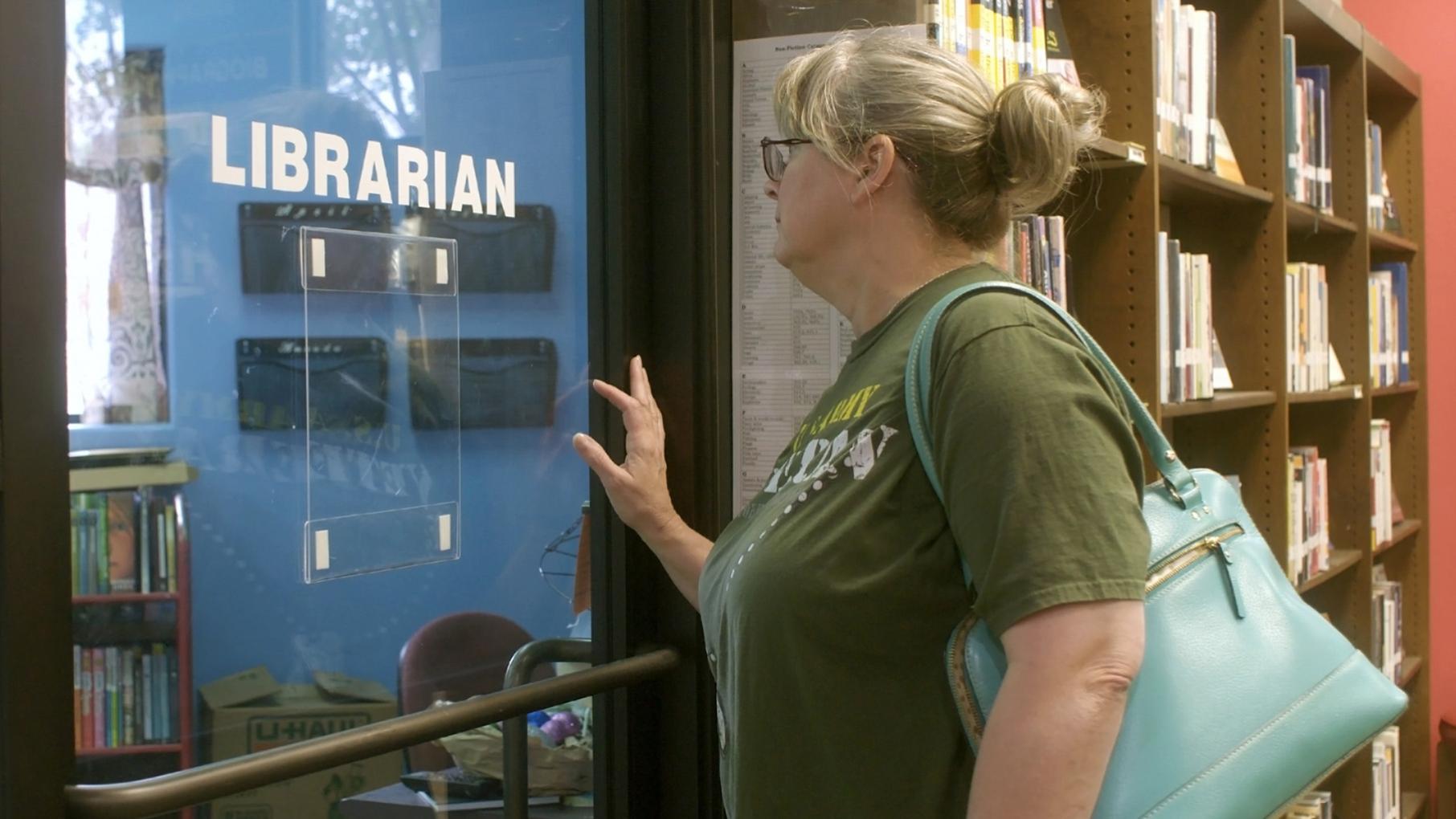 A woman stands in front of a door that says "Librarian" on it
