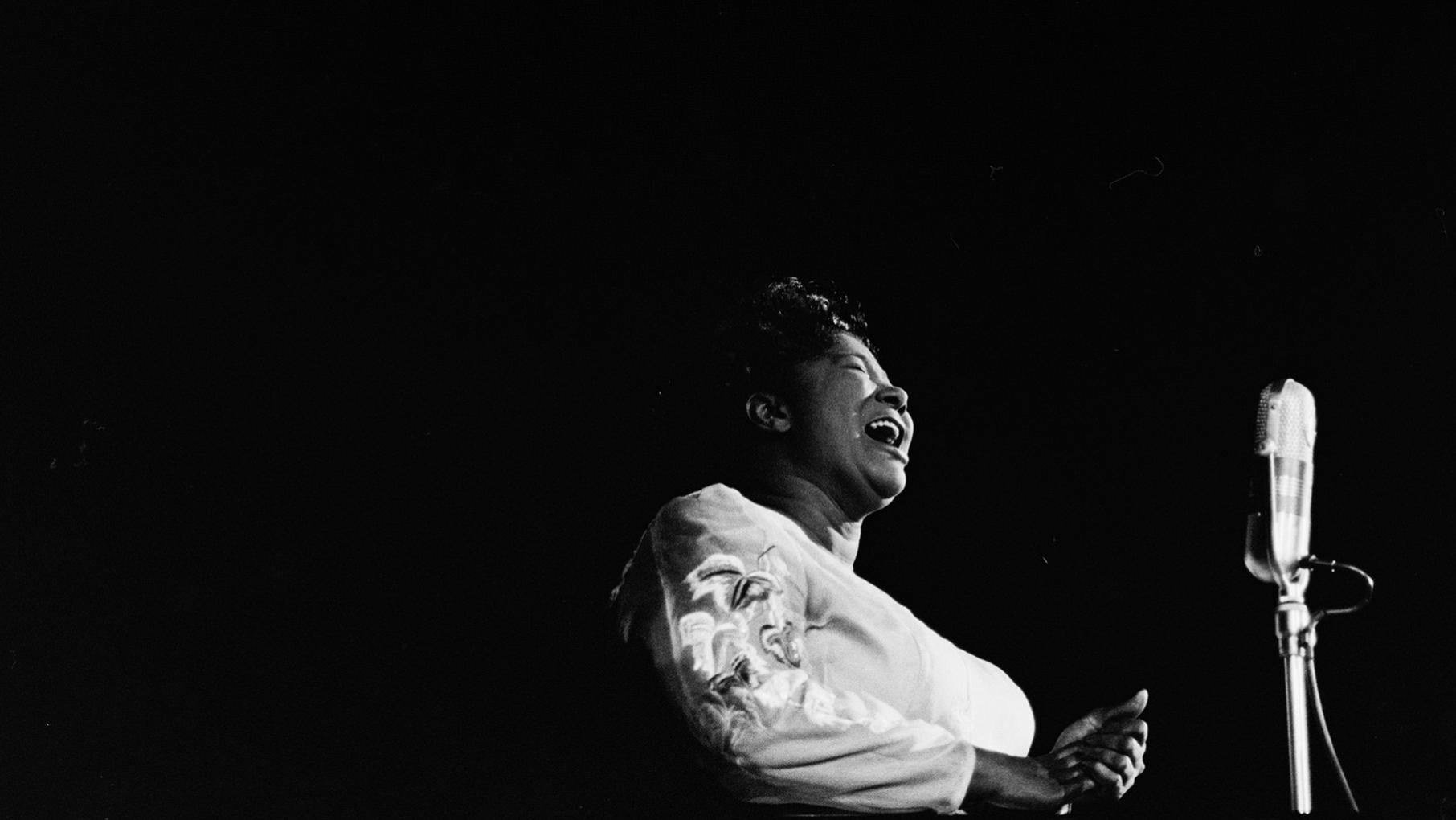 Mahalia Jackson at a microphone against a black background