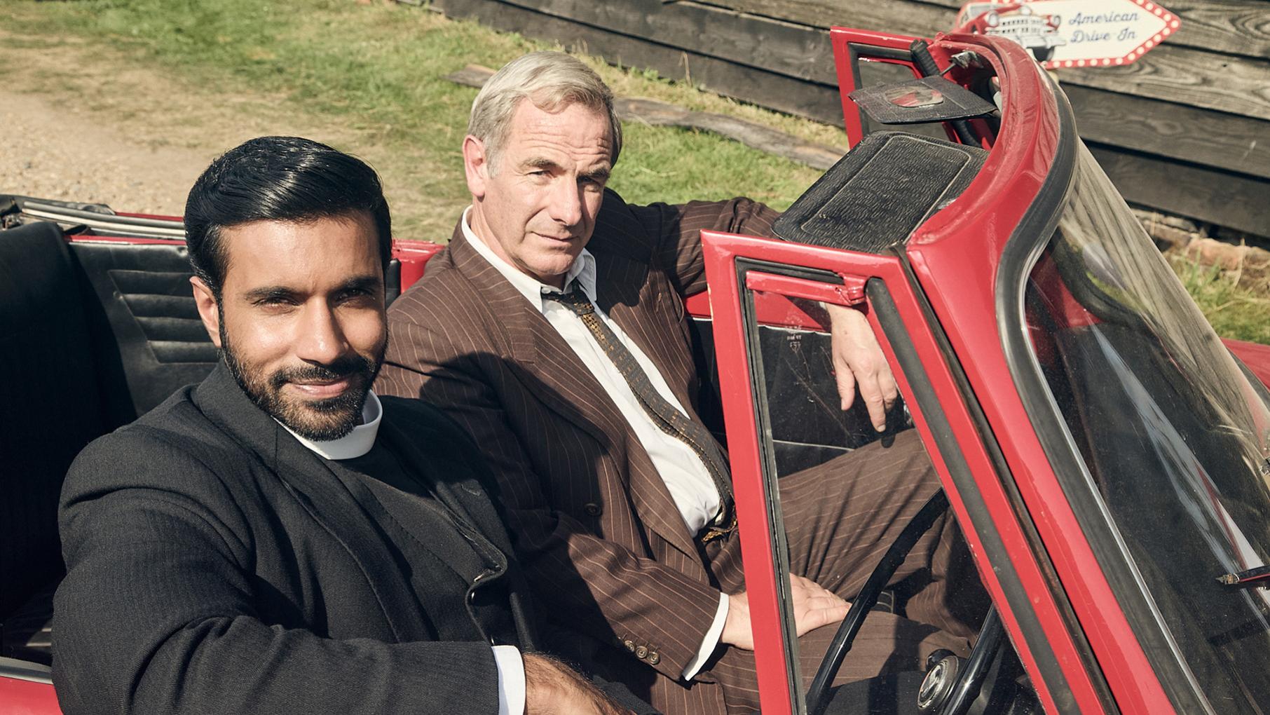 Alphy and Geordie sit in a red convertible with the top down