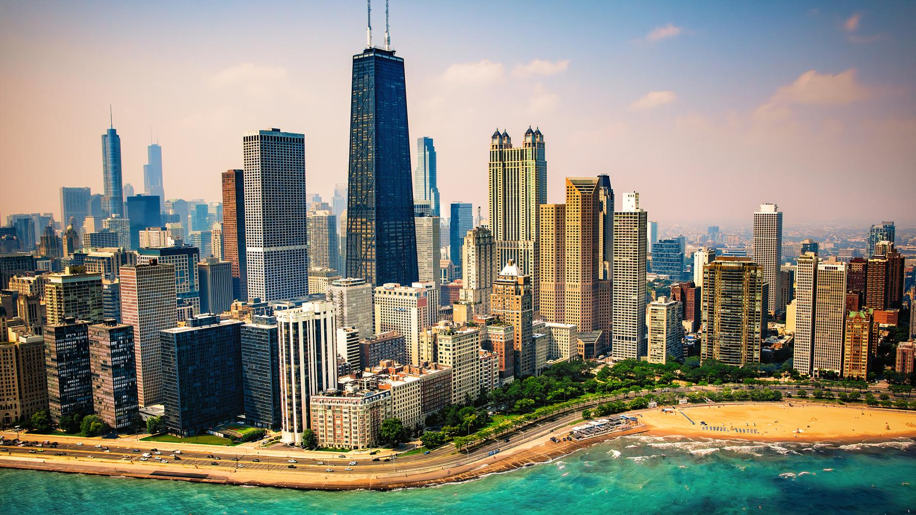 An aerial view of the city of Chicago, with Oak Street Beach and Lake Michigan in the foreground, looking east toward Hancock Tower and other skyscrapers