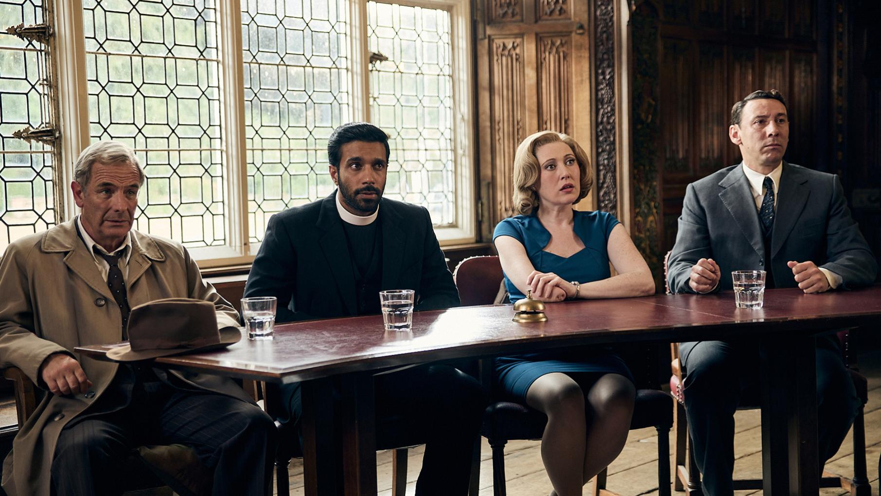 Geordie, Alphy, Miss Scott, and Leonard sit behind a table in an ornate hall