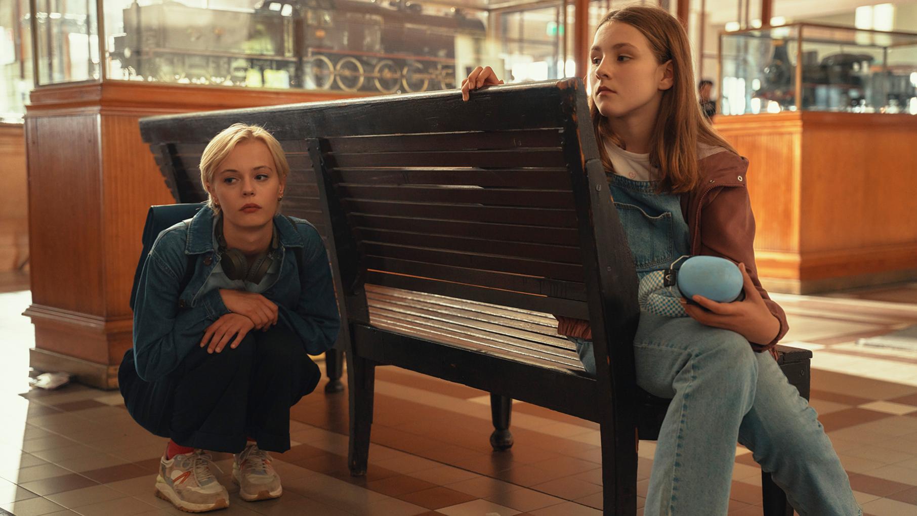 A girl sits on a bench while Patience squats behind it