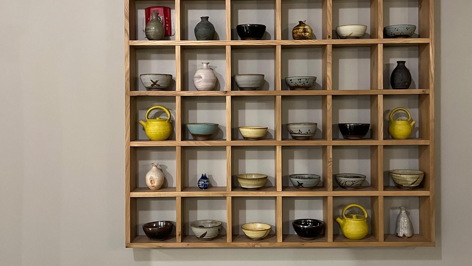 Ceramics on display in a square wooden grid mounted on a wall