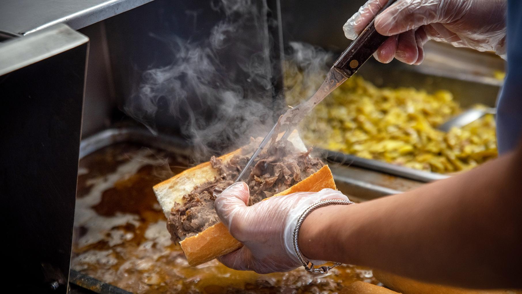 A worker at Johnnie's Beef topping a bun with Italian beef