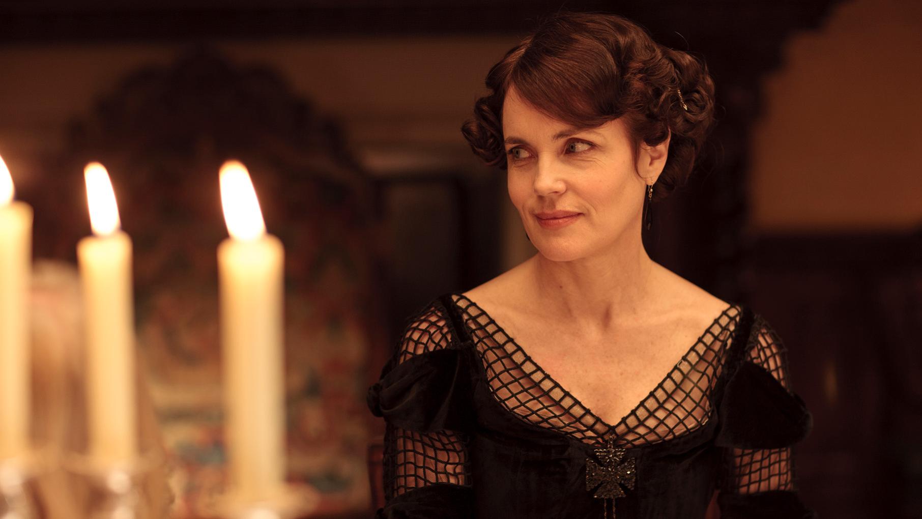 Cora sits at a table near candles in a black dress