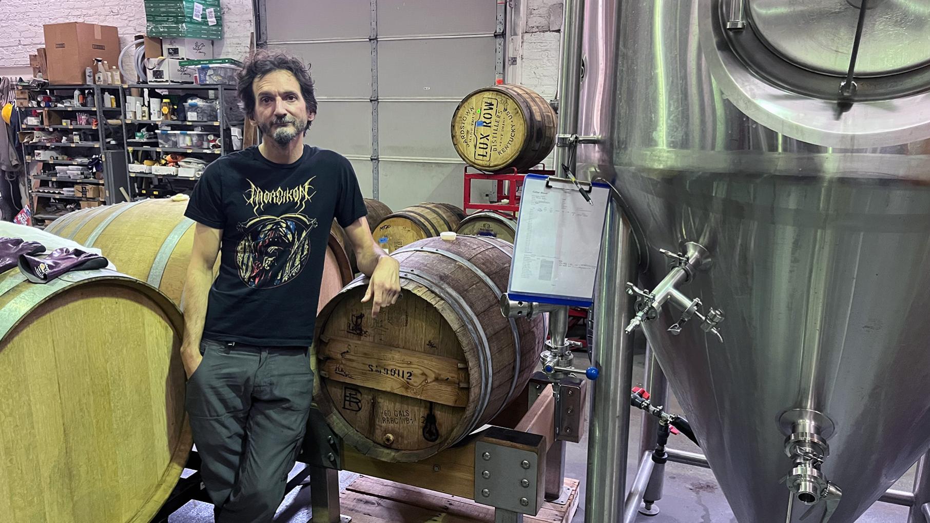 John Laffler stands with a hand on a barrel in a brewery space