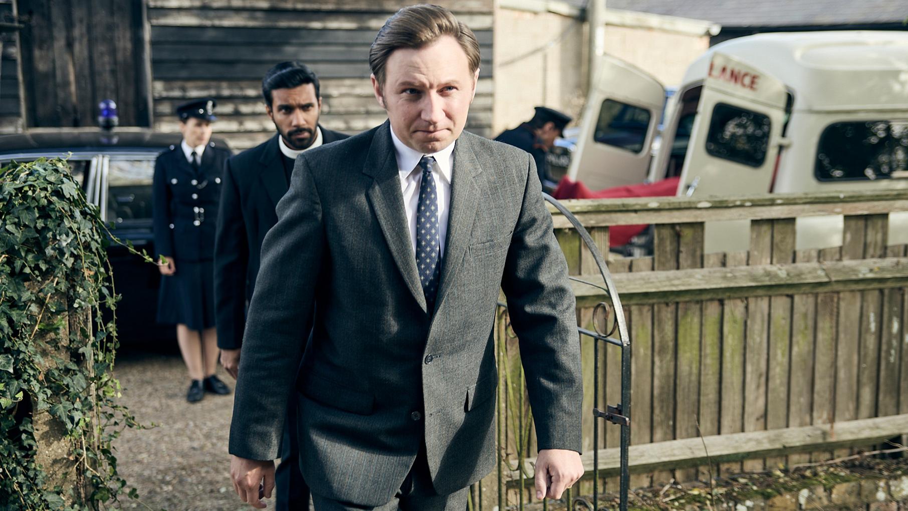 Larry marches through a yard with Alphy and policemen behind him