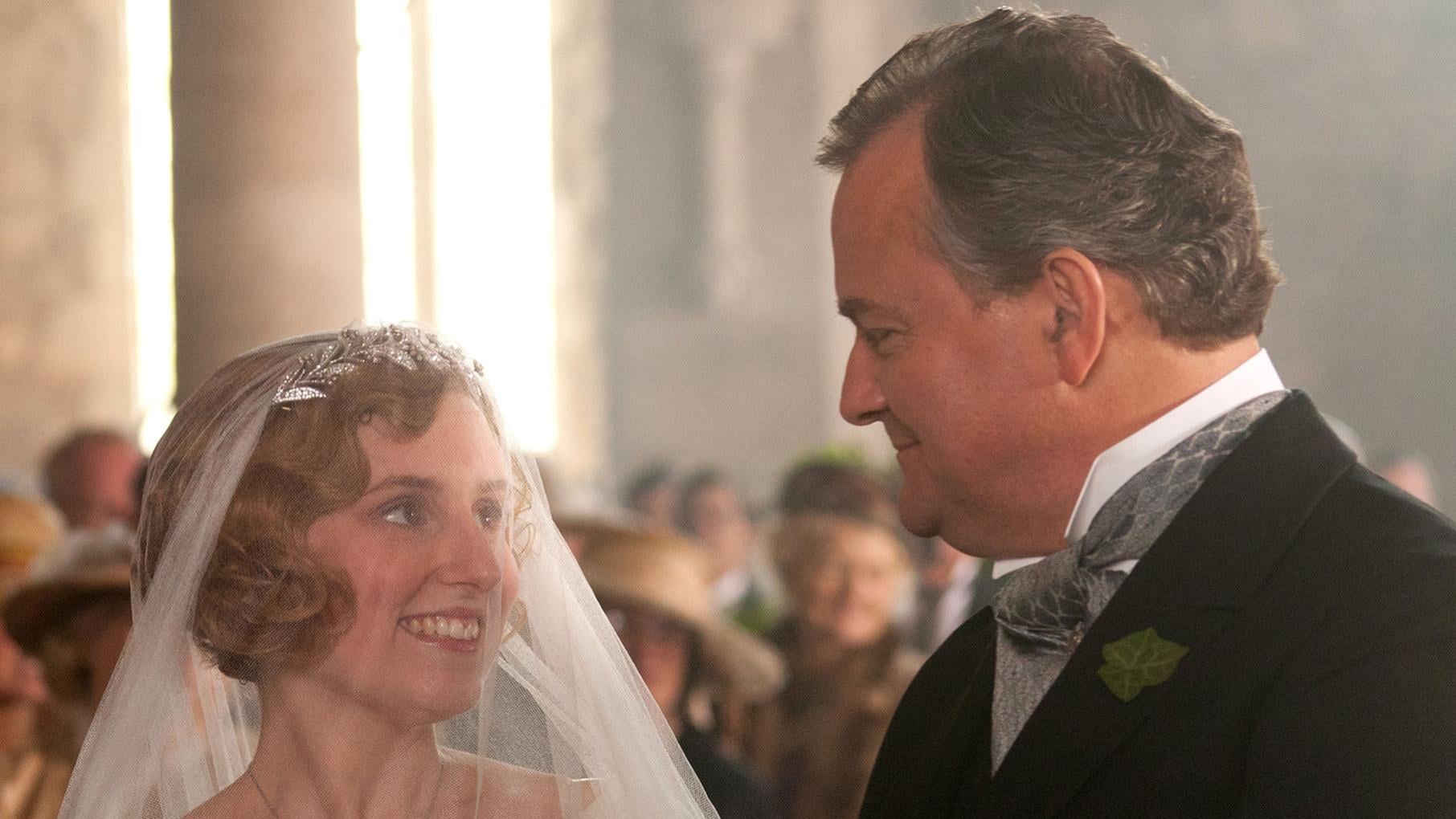Edith in a wedding veil smiles up at Robert in a tuxedo
