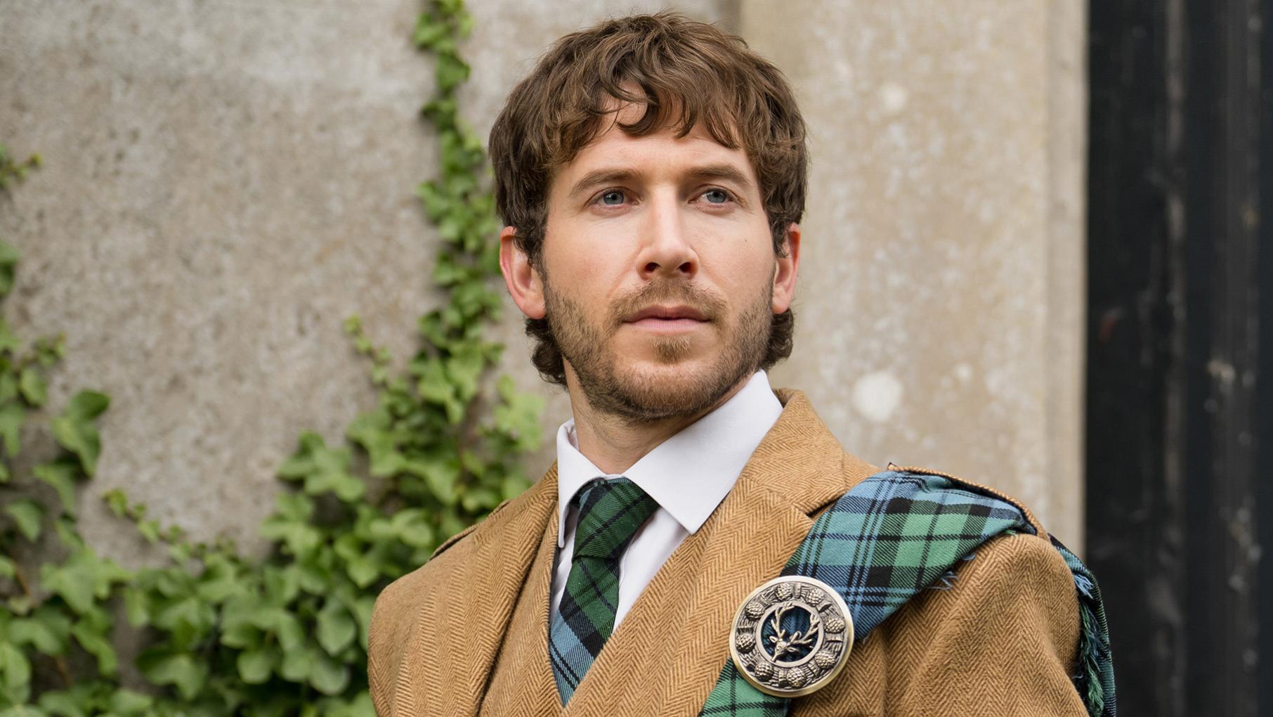 Alasdair outside in a tweed outfit with a tartan sash and tie