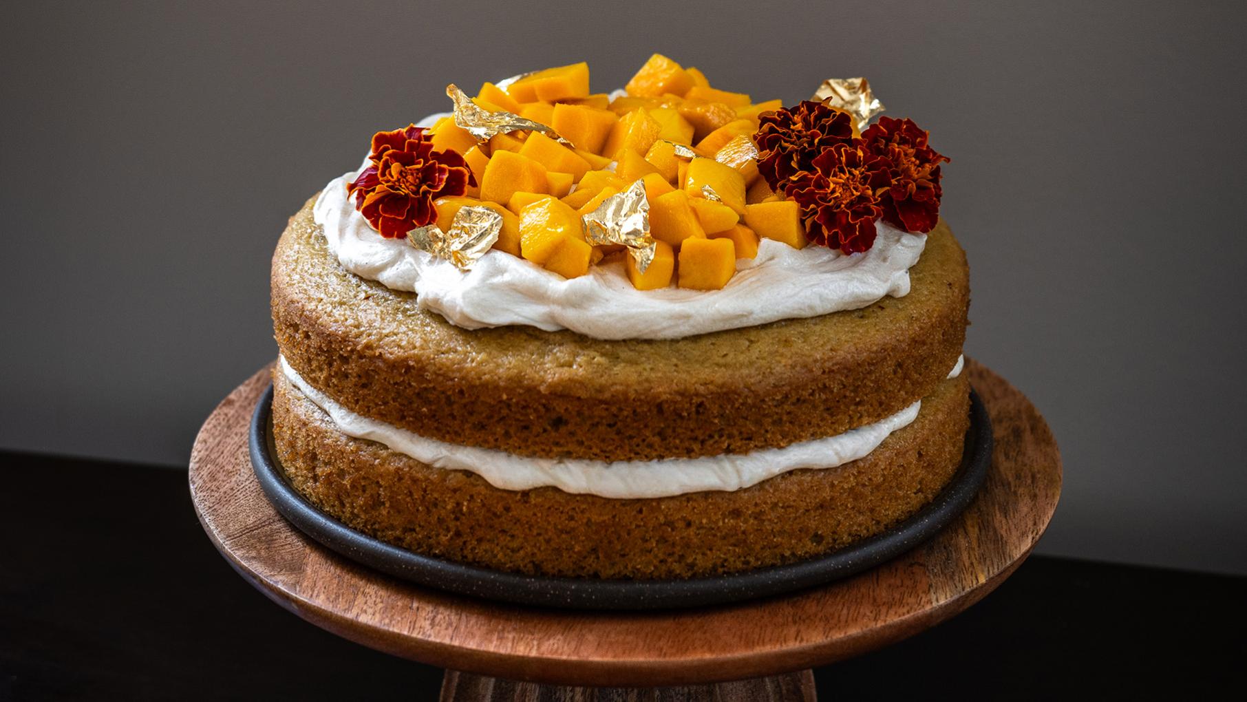A layered cake topped with mangos, gold leaf, and marigolds