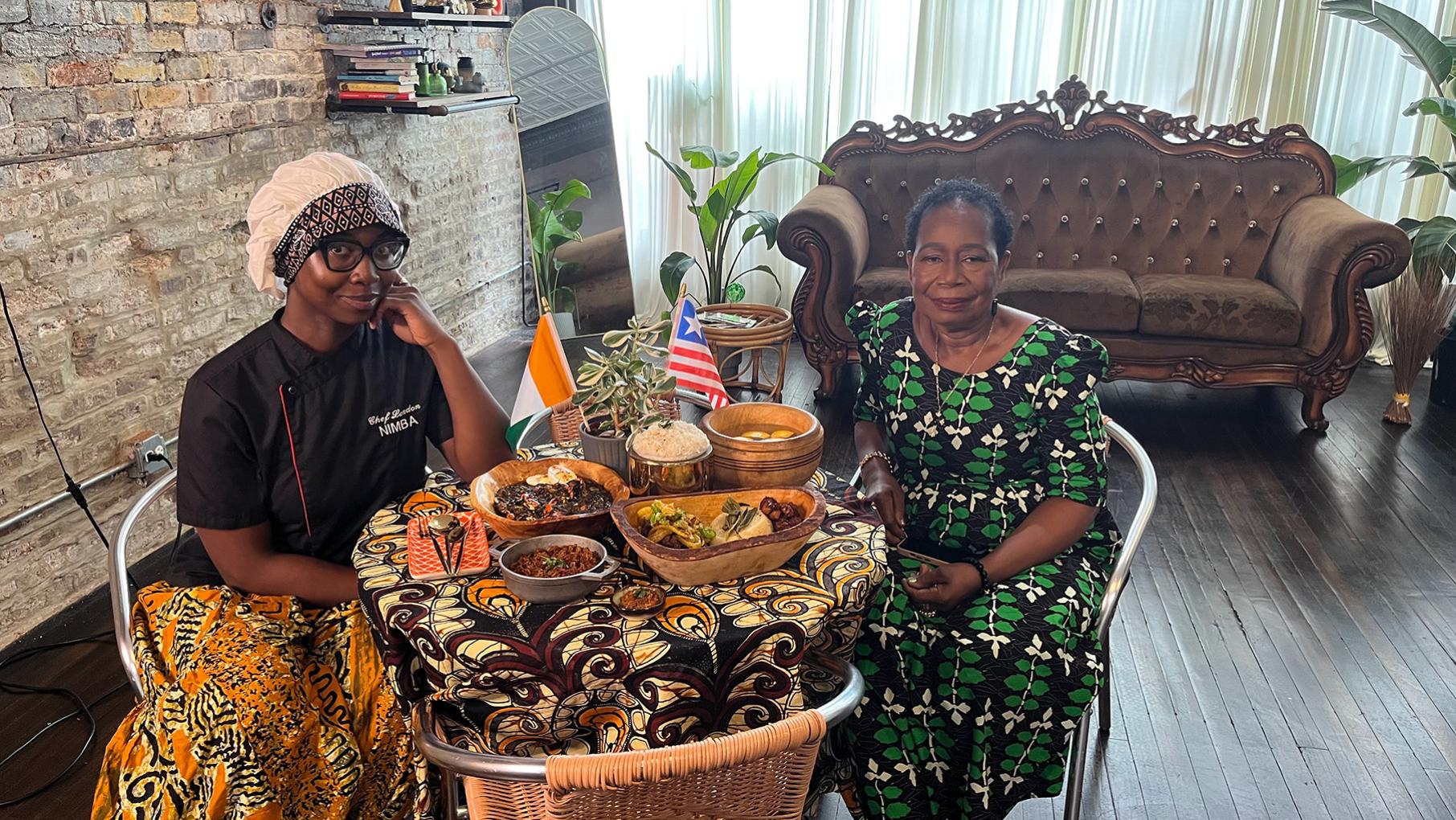 A woman and her granddaughter sit at a table loaded with food