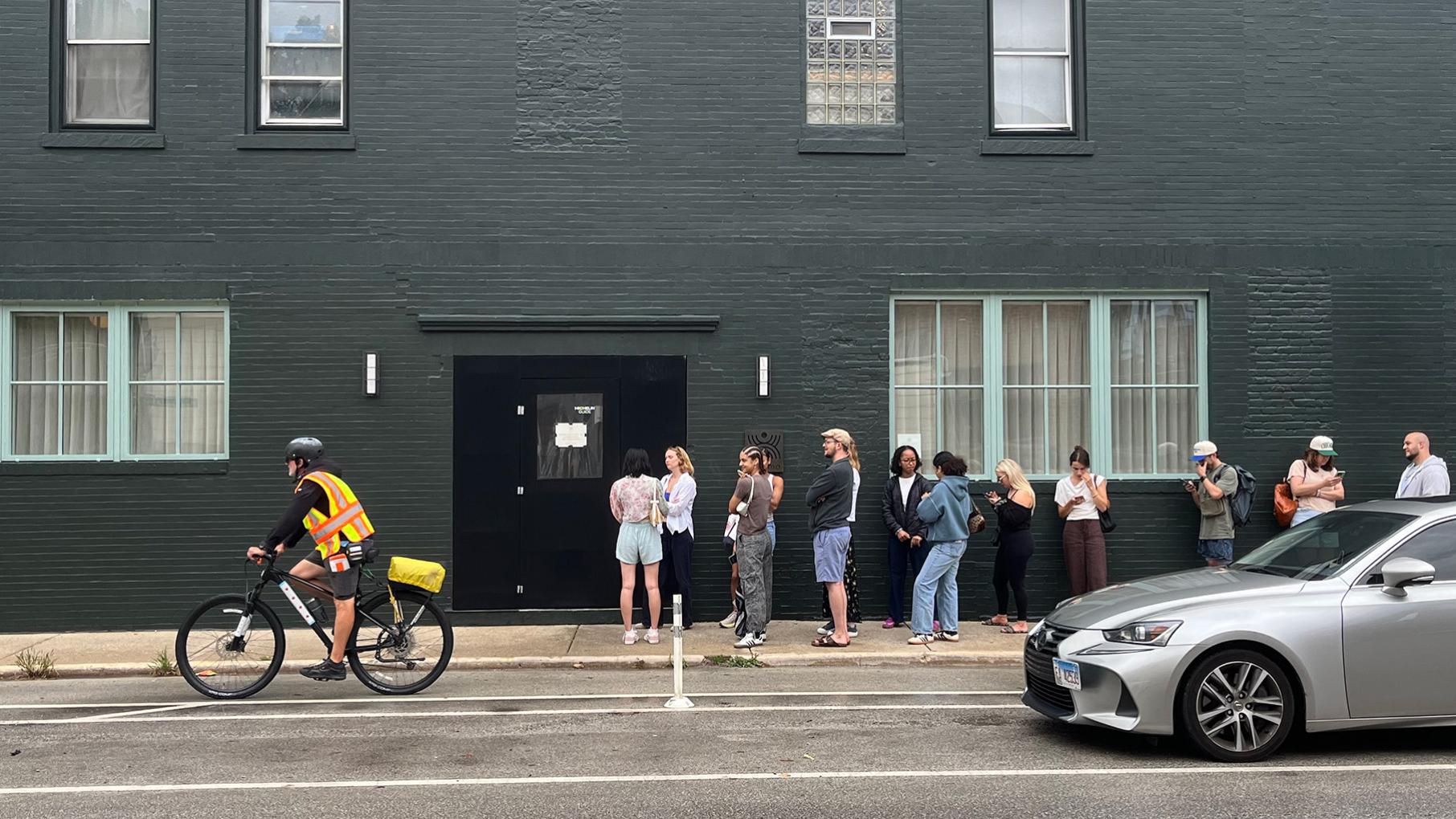 A biker rides past a line in front of a building