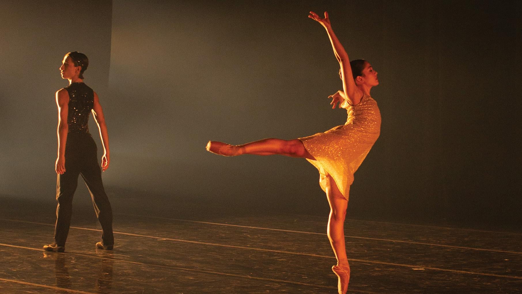 A ballet dancer en pointe and another dancer standing behind them on stage