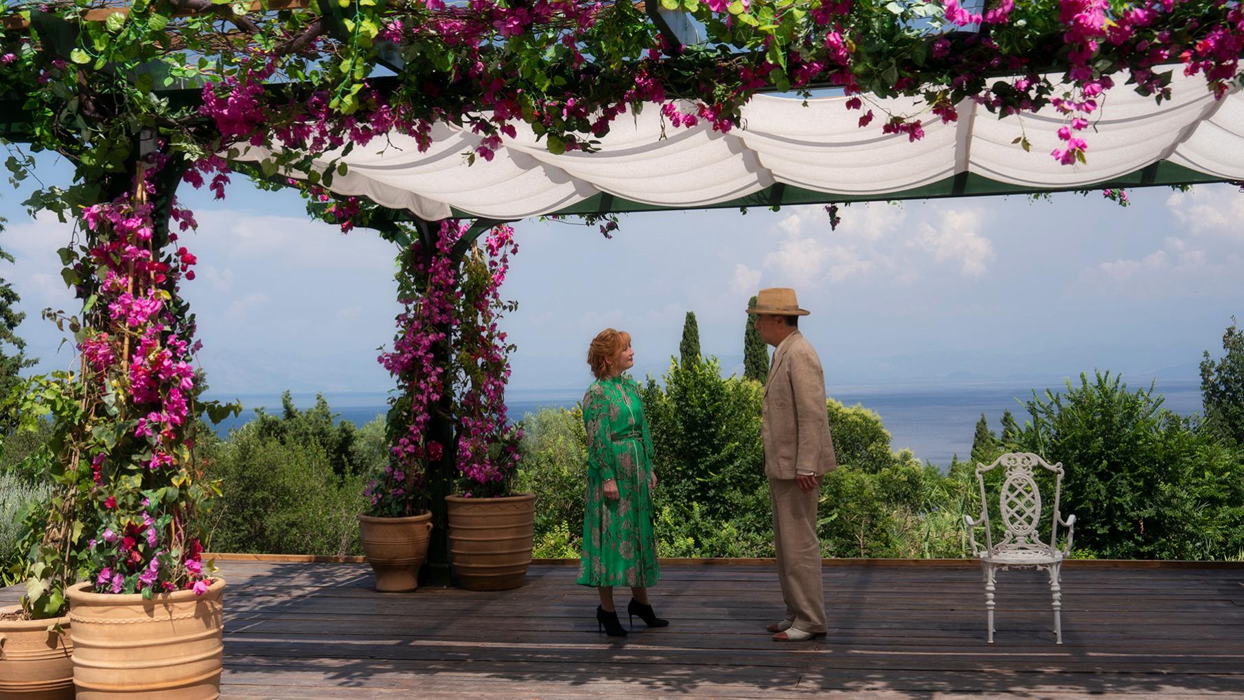 Susan and Atticus stand near the ocean on a patio under covered pergola