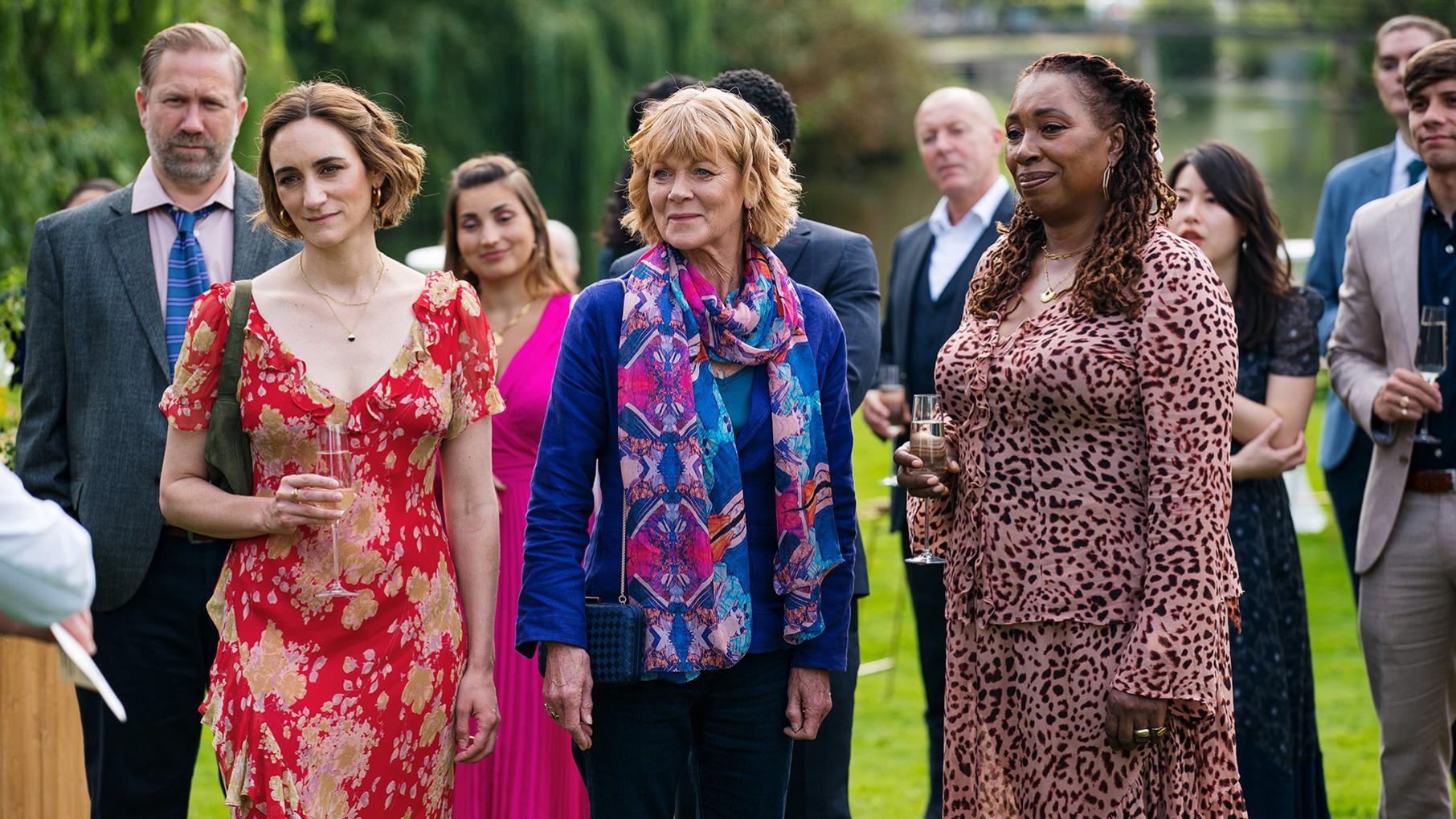 Judith, Becks, and Suzie stand amongst a crowd on a lawn
