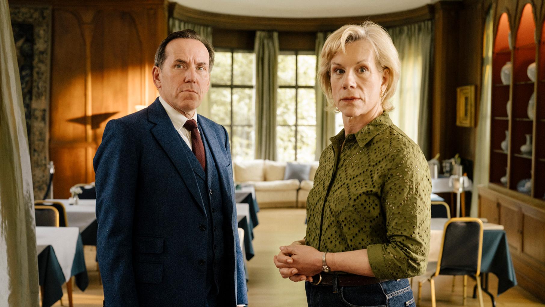 Professor T and Dr. Goldberg stand in a nice room half-facing each other and the camera