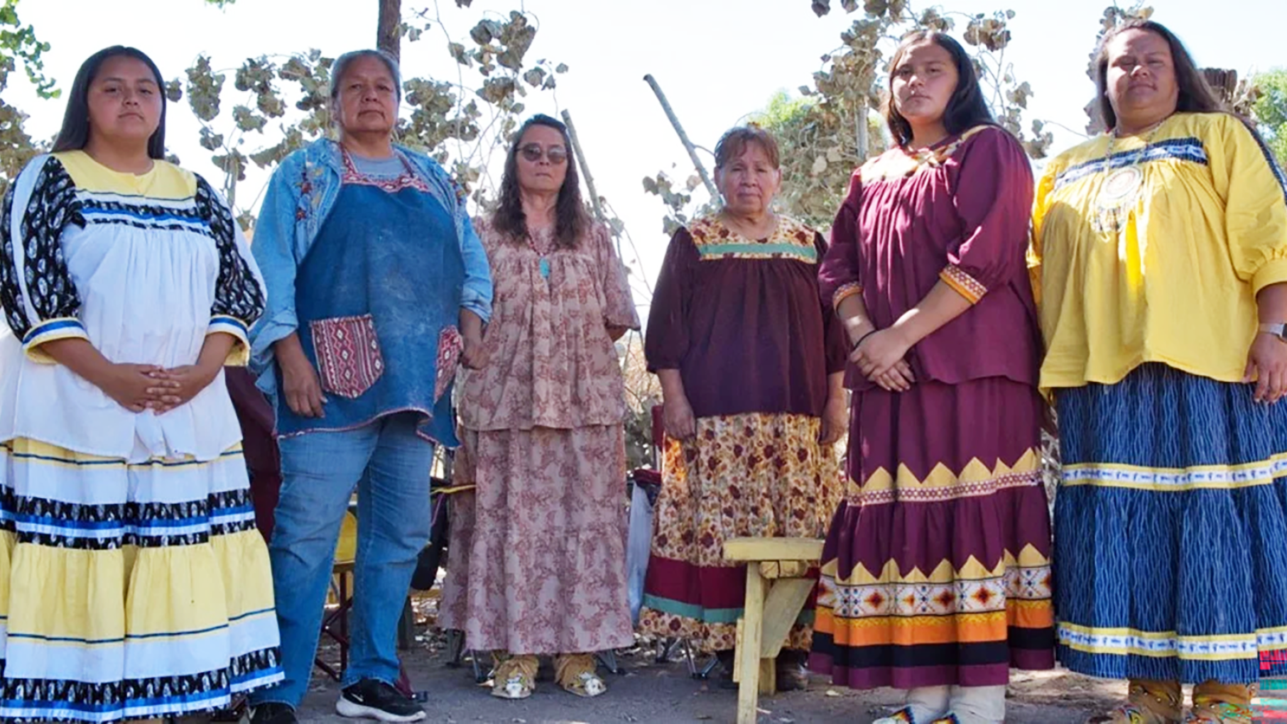 Six indigenous women in colorful skirts pose for the camera