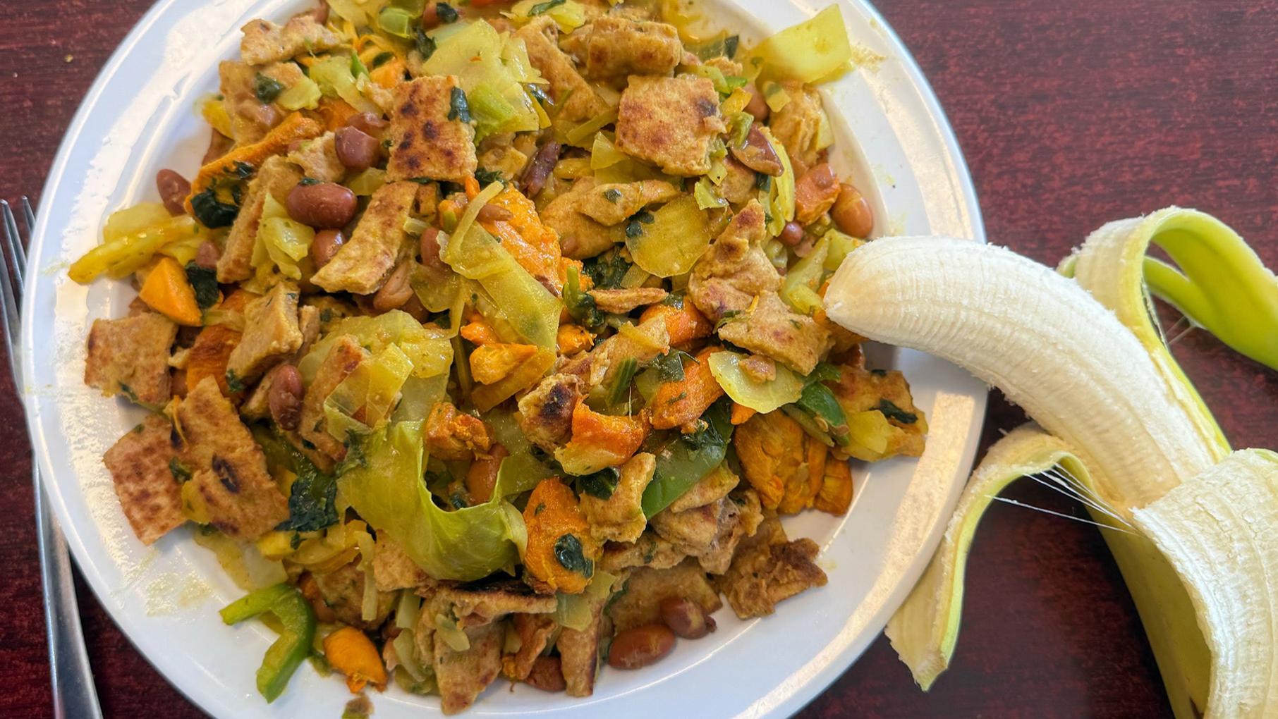 A plate of chopped vegetables and meat with a half-peeled banana resting on the side