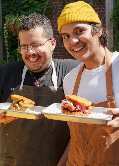 Alejandro “Ale” Gonzalez and Enrique “Quique” Ortiz laugh while holding trays with jibaritos