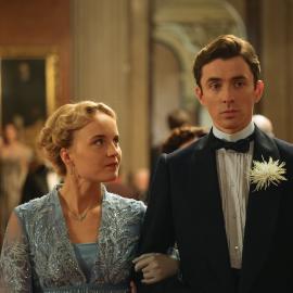 Clara looks at Max in a tuxedo while she holds his arm