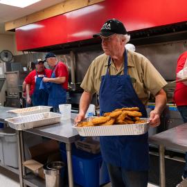 Man in kitchen carrying tray of fish fries