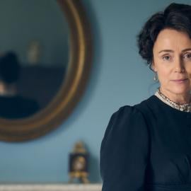 Cassandra Austen stands in front of a mirror on a wall and looks at the camera