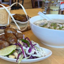 Several plates of Lao food, including sausage and a bowl of soup