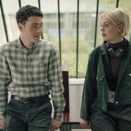 Elliot and Patience sit next to each other on a table and look at each other