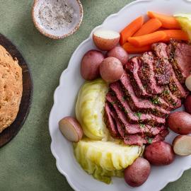 A platter of sliced corned beef, cabbage, potatoes, and carrots next to a loaf of soda bread