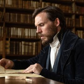 Edmond sits in a nice jacket in a library reading an old letter
