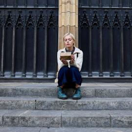 Patience sits on the steps of a cathedral holding a box