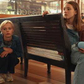 A girl sits on a bench while Patience squats behind it