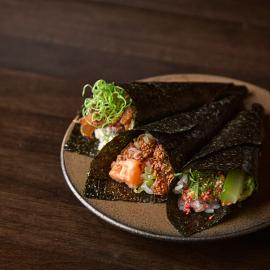 Three handrolls lie on a plate on a dark wood surface