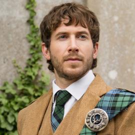 Alasdair outside in a tweed outfit with a tartan sash and tie
