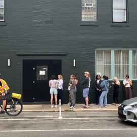 A biker rides past a line in front of a building