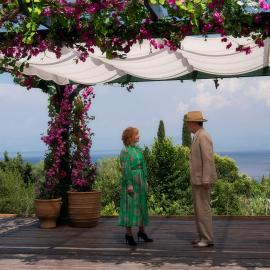 Susan and Atticus stand near the ocean on a patio under covered pergola