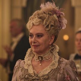 Ann Forsyte smiles lightly in evening wear at a party in soft golden light