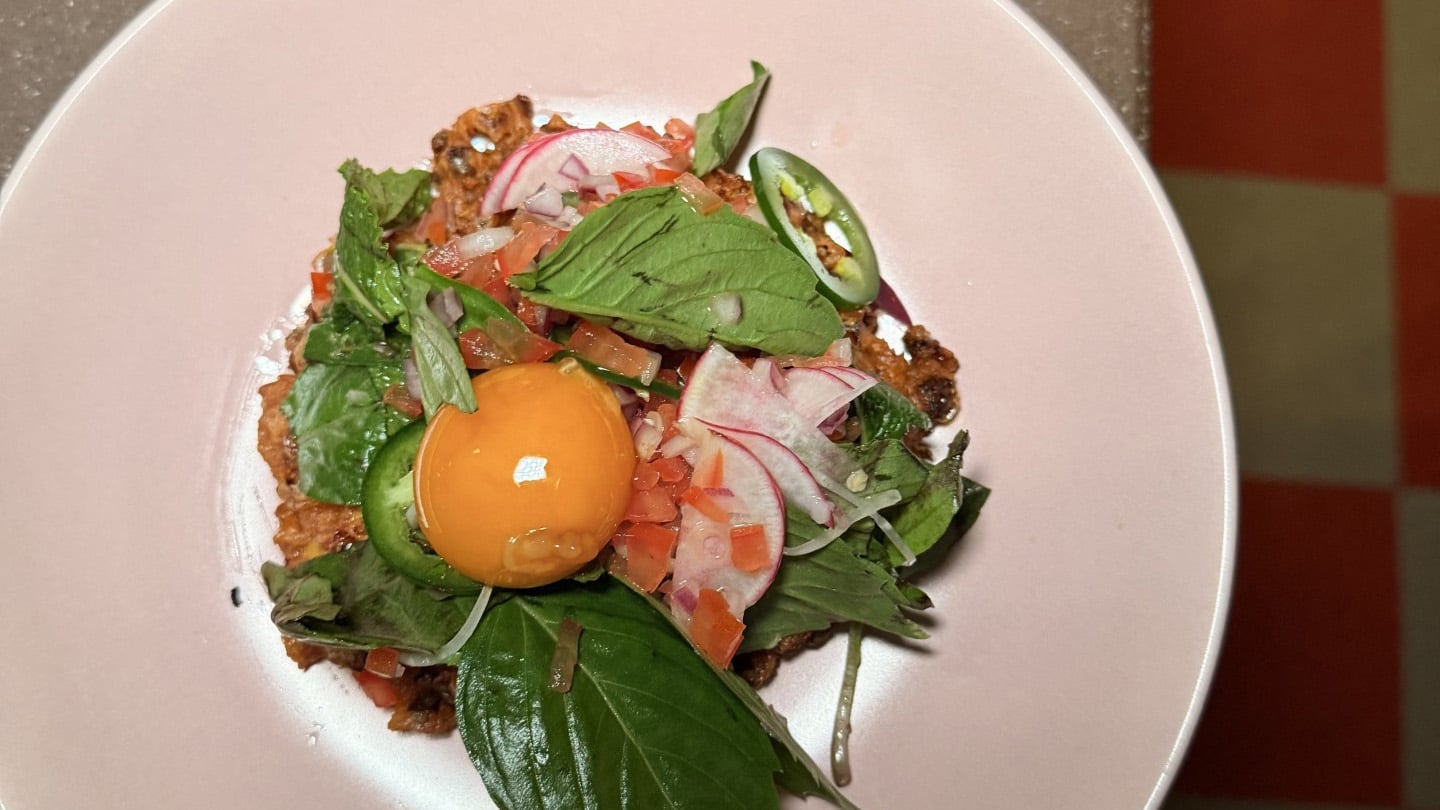 A plate with ground meat, herbs, an egg yolk, and more on it
