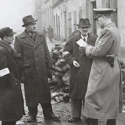 A German policeman checks the identification papers of Jewish people in the Krakow ghetto. Poland. Circa 1941. Photo: Courtesy National Archives in Krakow