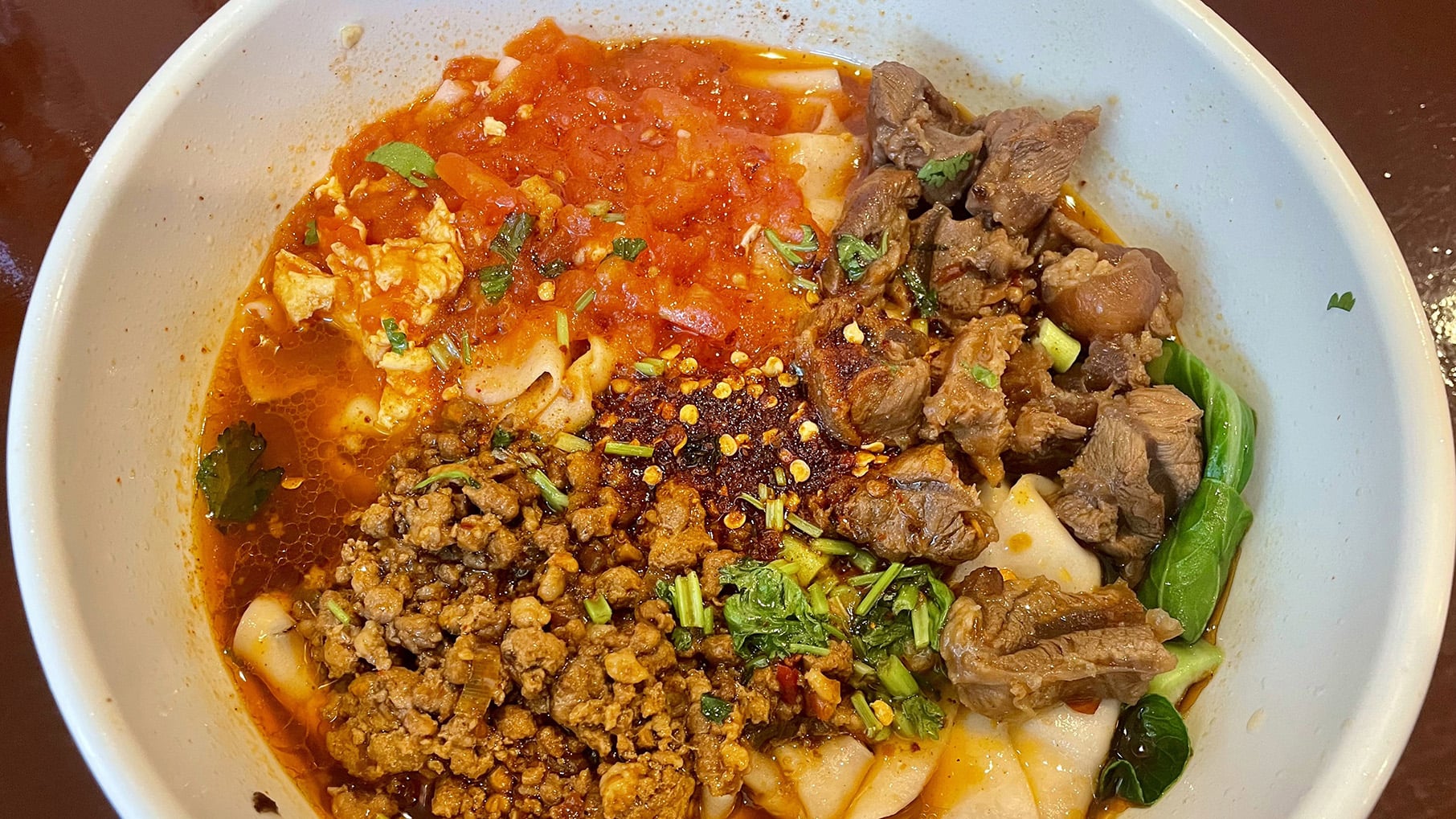 A bowl with noodles, meat, tomatoes, and more